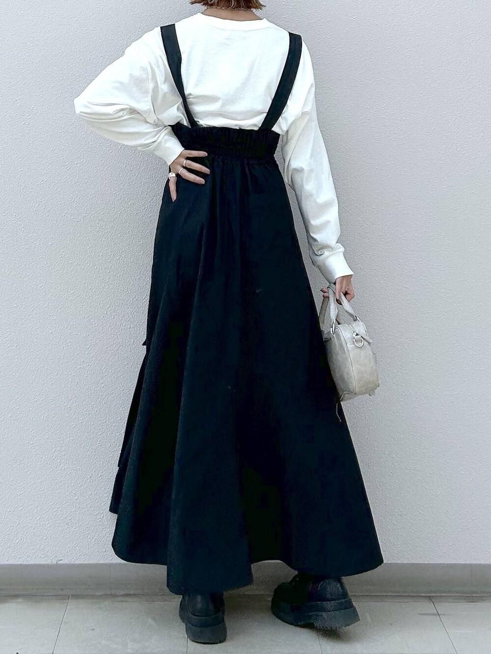 ホワイト系のTシャツ/カットソー、ブラック系のブーツ、ブラック系のジャンパースカートを着用したレディースの冬コーディネートの5枚目の写真