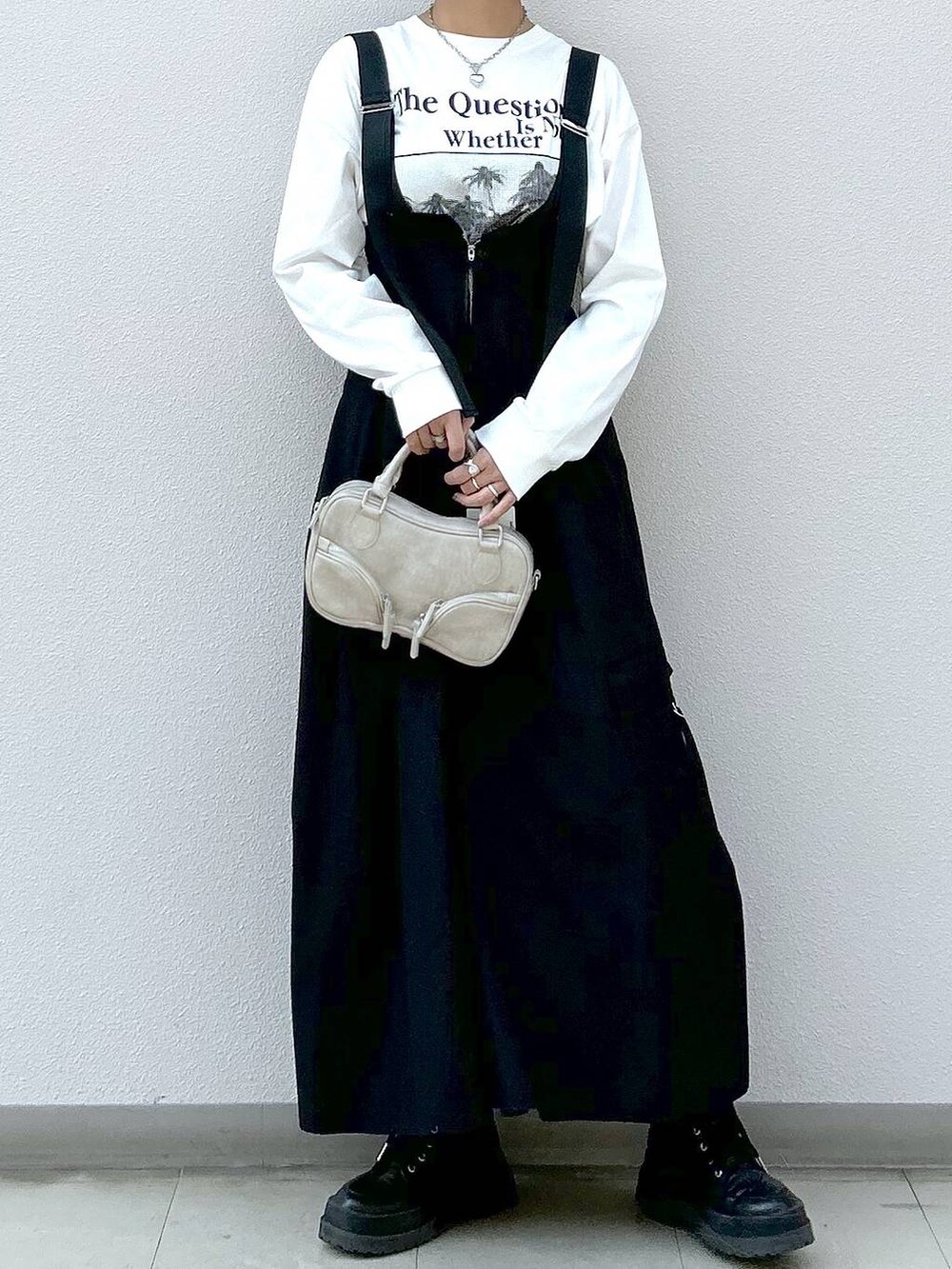 ホワイト系のTシャツ/カットソー、ブラック系のブーツ、ブラック系のジャンパースカートを着用したレディースの冬コーディネートの3枚目の写真