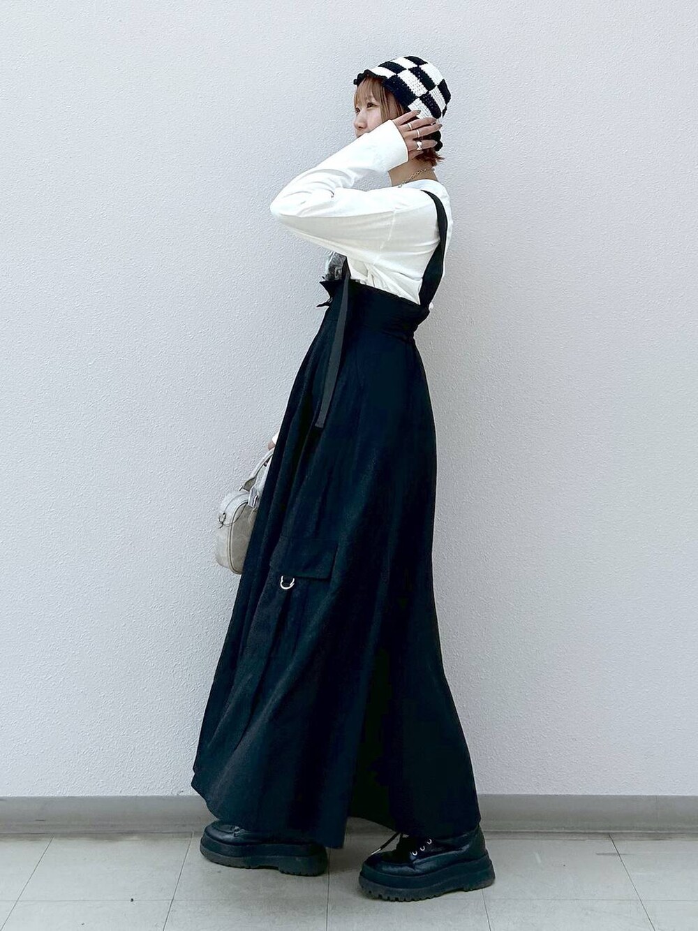 ホワイト系のTシャツ/カットソー、ブラック系のブーツ、ブラック系のジャンパースカートを着用したレディースの冬コーディネートの2枚目の写真