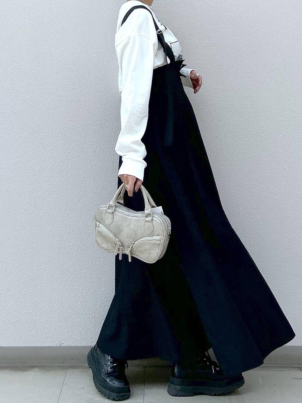 ホワイト系のTシャツ/カットソー、ブラック系のブーツ、ブラック系のジャンパースカートを着用したレディースの冬コーディネートの4枚目の写真