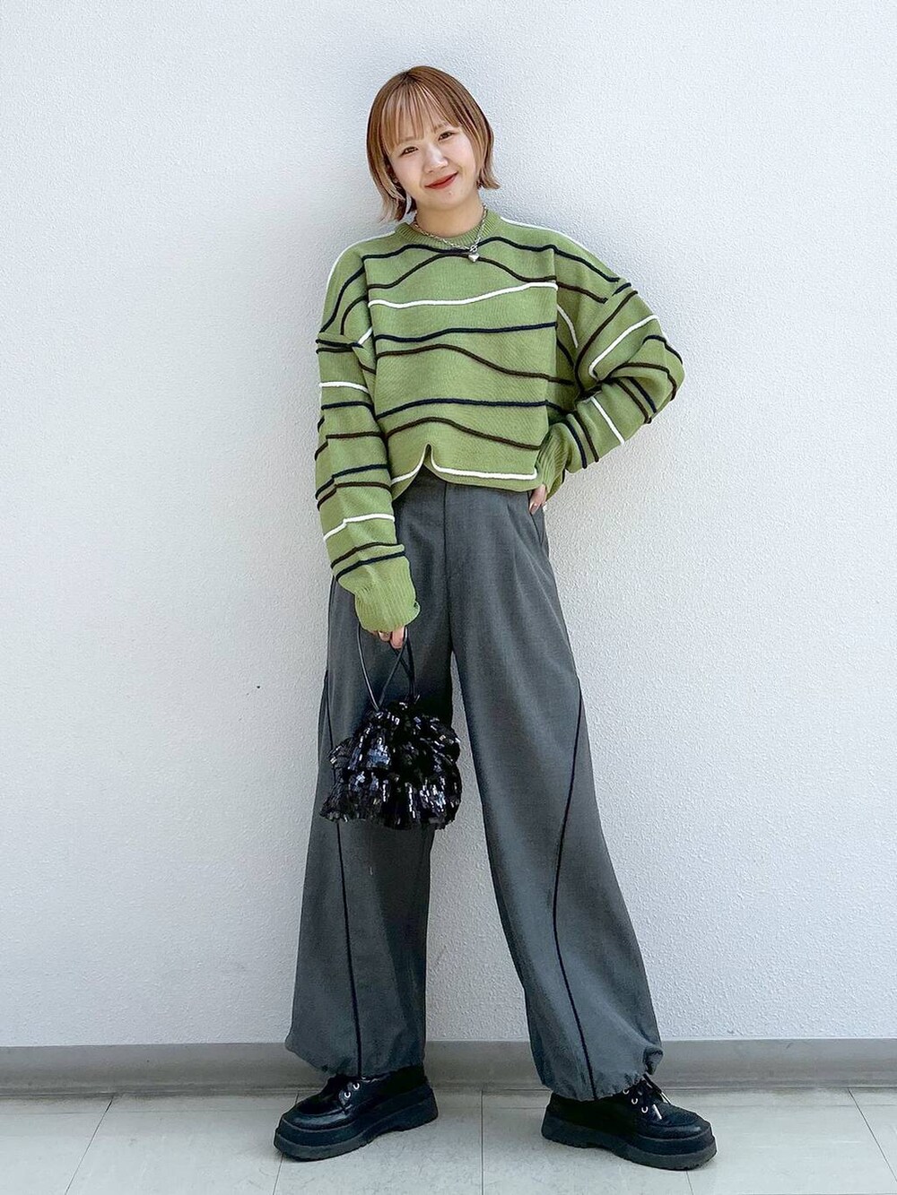 グレー系のその他パンツ、ブラック系のブーツ、グリーン系のニット/セーターを着用したレディースの冬コーディネートの7枚目の写真