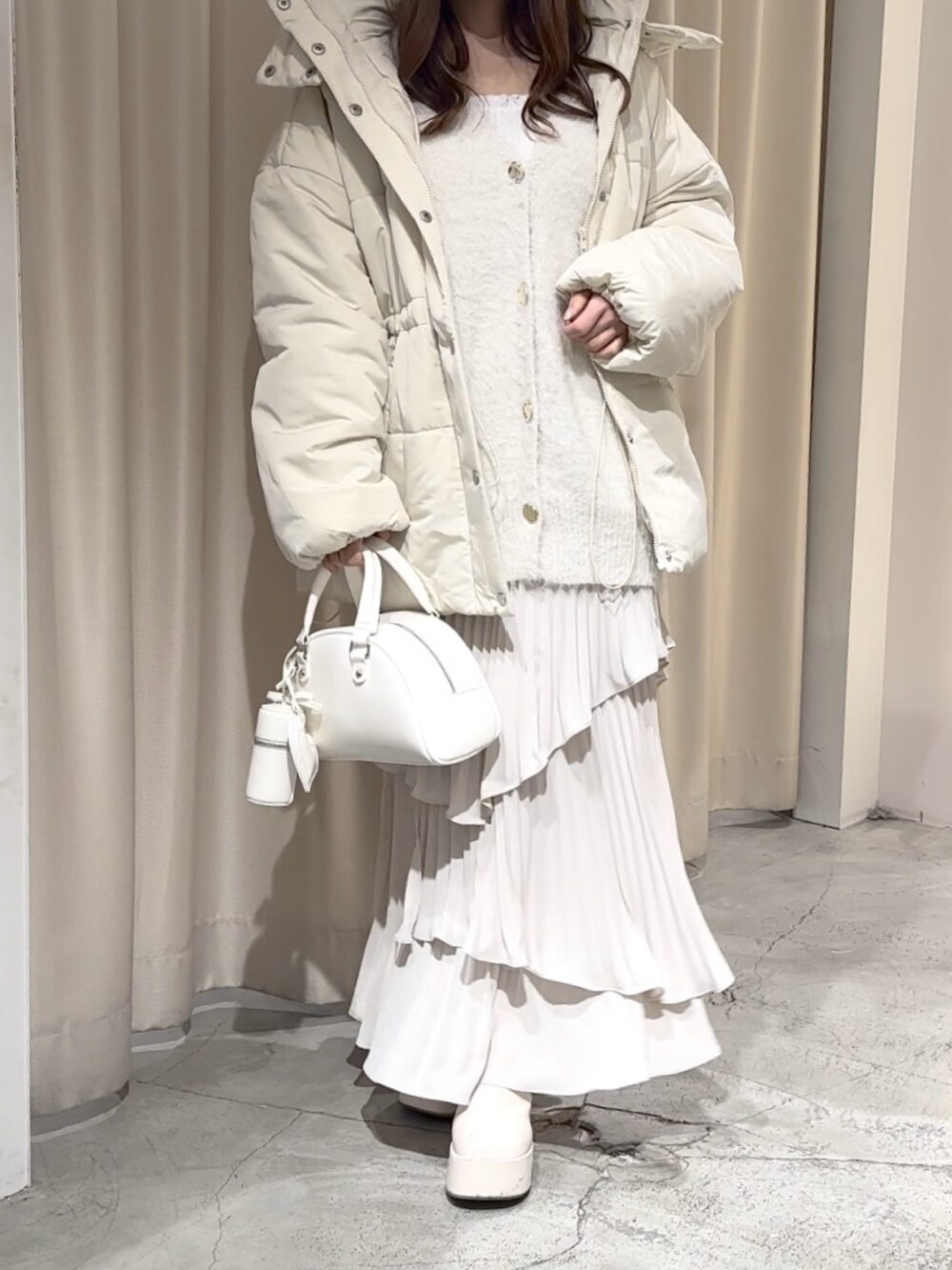 ホワイト系のカーディガン/ボレロ、イエロー系のダウンジャケット/コート、ホワイト系のスカートを着用したレディースの冬コーディネートの3枚目の写真