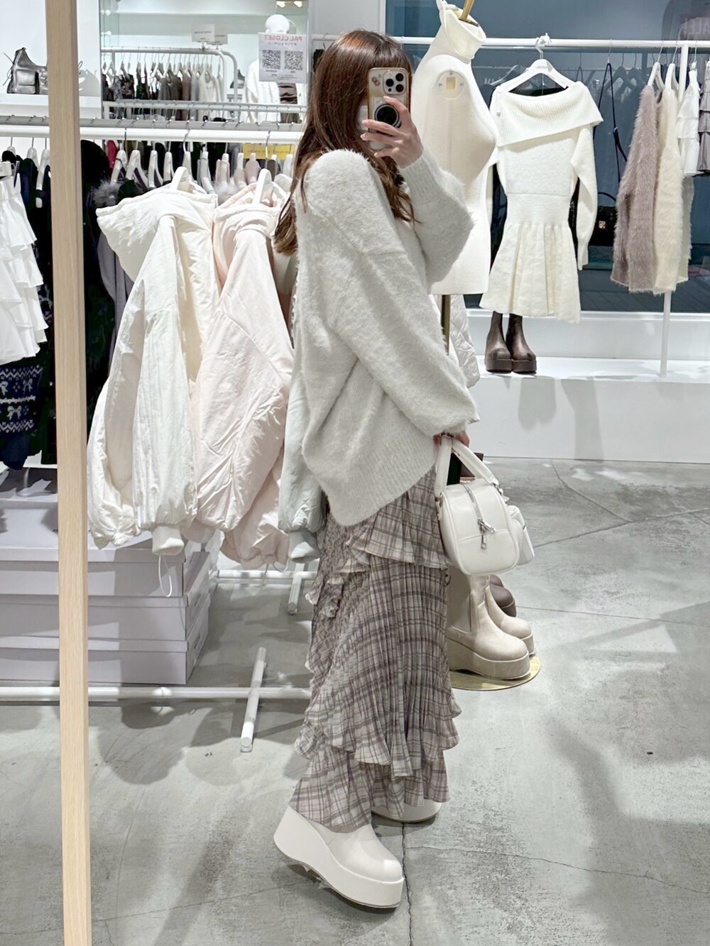 ホワイト系のハンドバッグ、ホワイト系のカーディガン/ボレロ、ブラウン系のスカートを着用したレディースの冬コーディネートの2枚目の写真