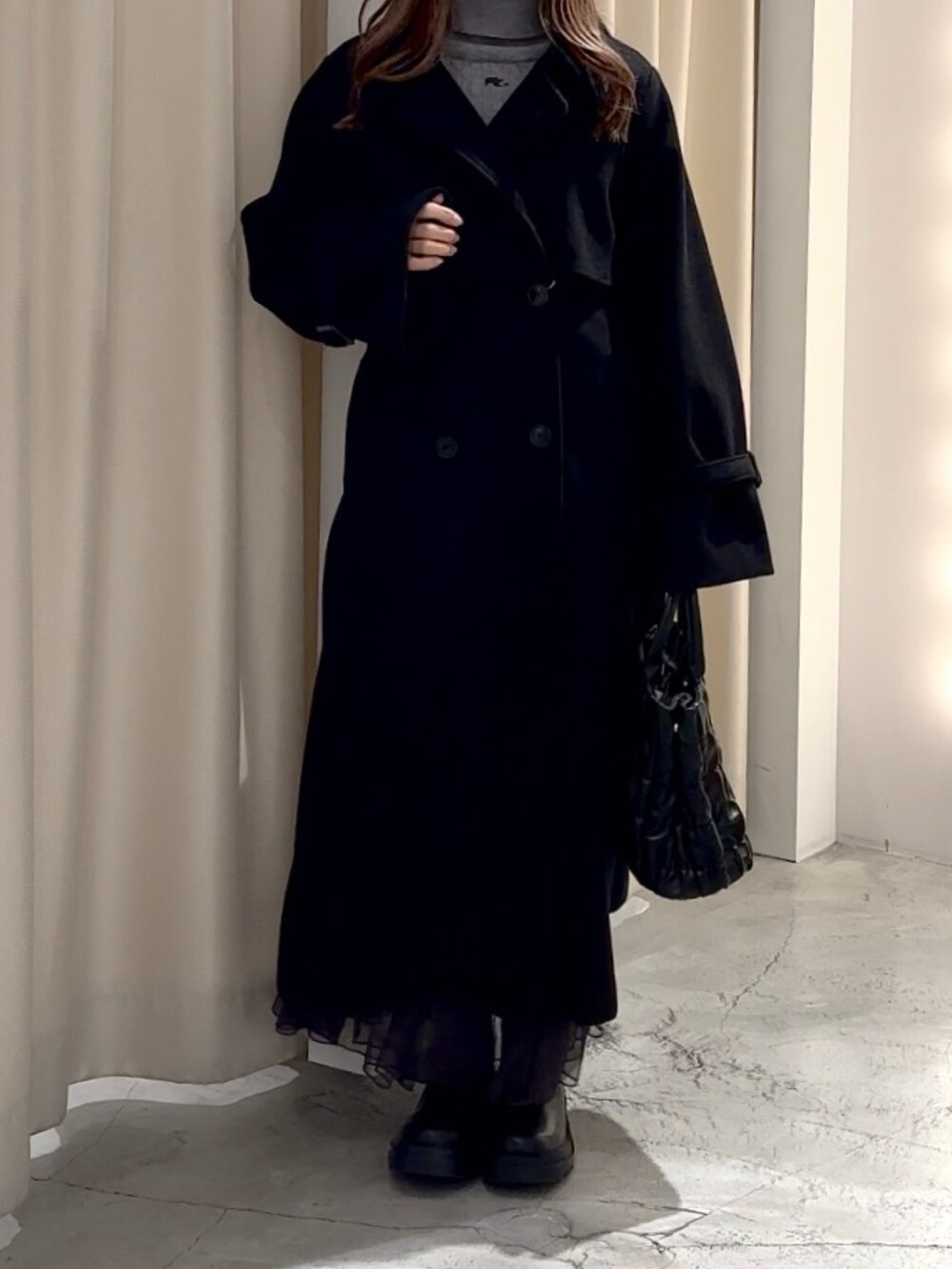 グレー系のニット/セーター、ブラック系のステンカラーコートを着用したレディースの冬コーディネートの2枚目の写真