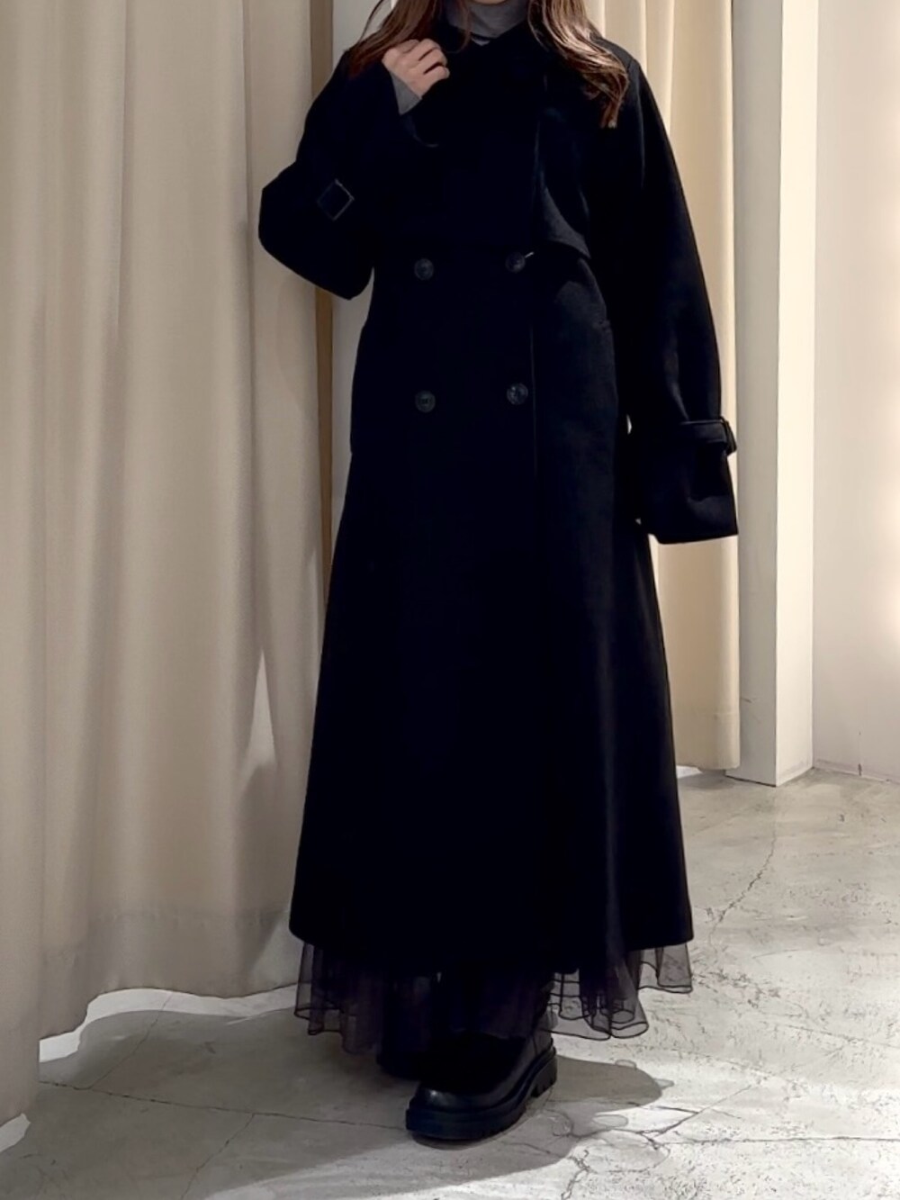 グレー系のニット/セーター、ブラック系のステンカラーコートを着用したレディースの冬コーディネートの3枚目の写真