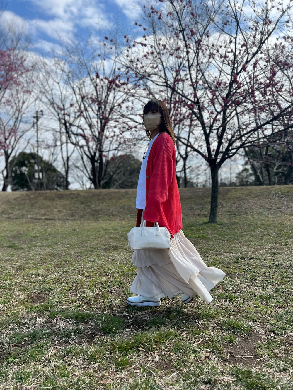 オレンジ系のカーディガン/ボレロ、ホワイト系のスカート、ホワイト系のローファーを着用したレディースの春コーディネートの3枚目の写真