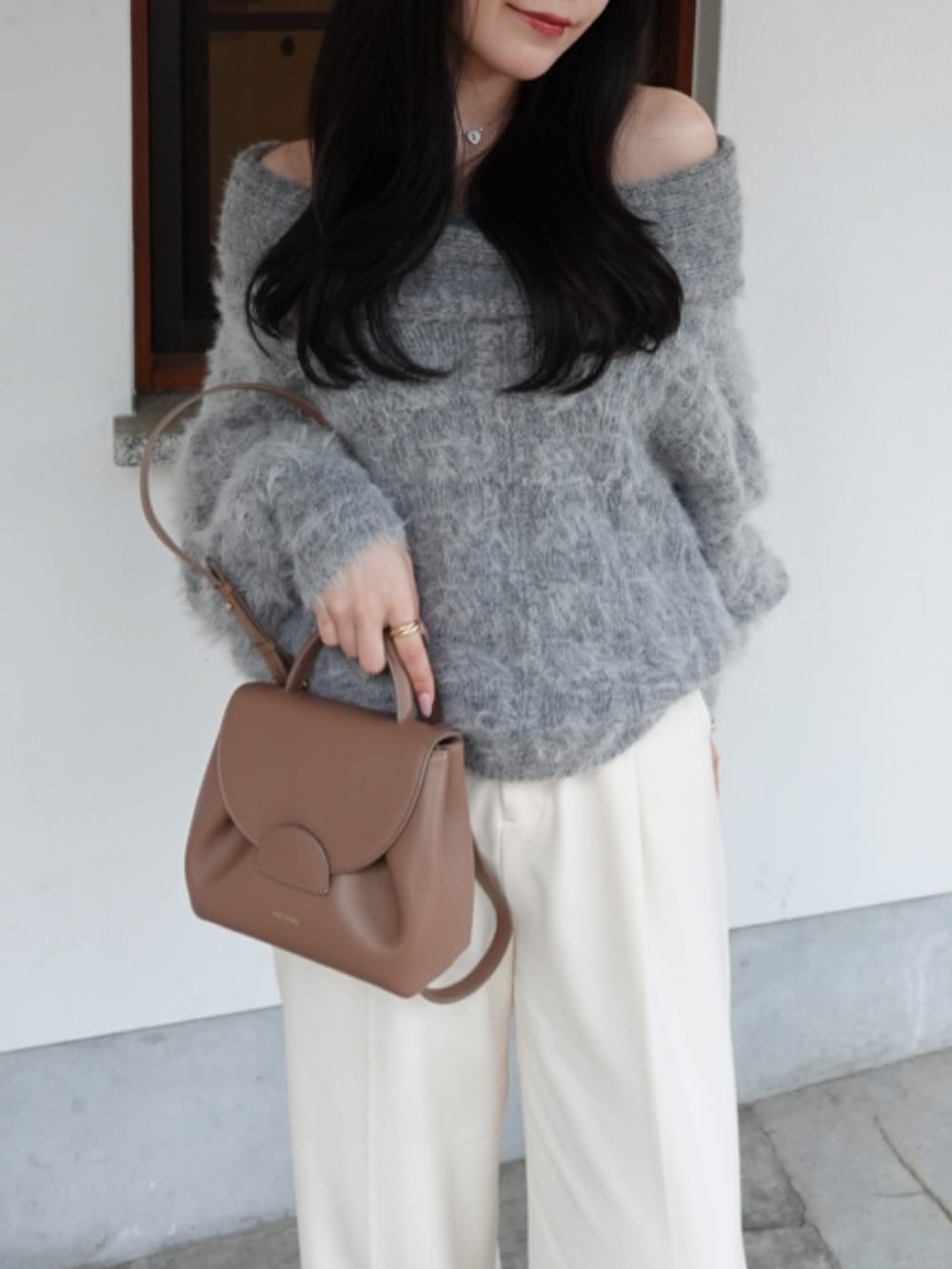 グレー系のニット/セーター、ブラウン系のハンドバッグ、ホワイト系のスラックスを着用したレディースの冬コーディネートの3枚目の写真