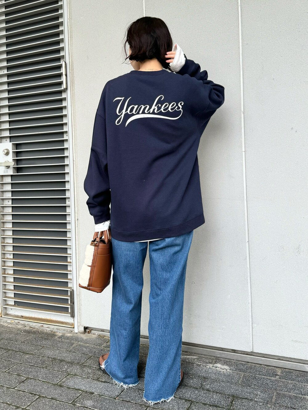 ブラウン系のバッグ、ブルー系のスウェット、ブルー系のデニムパンツを着用したレディースの秋コーディネートの3枚目の写真