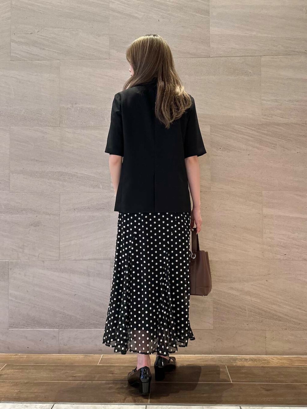 ブラック系のパンプス、ブラウン系のハンドバッグ、ブラック系のスカートを着用したレディースの春コーディネートの4枚目の写真