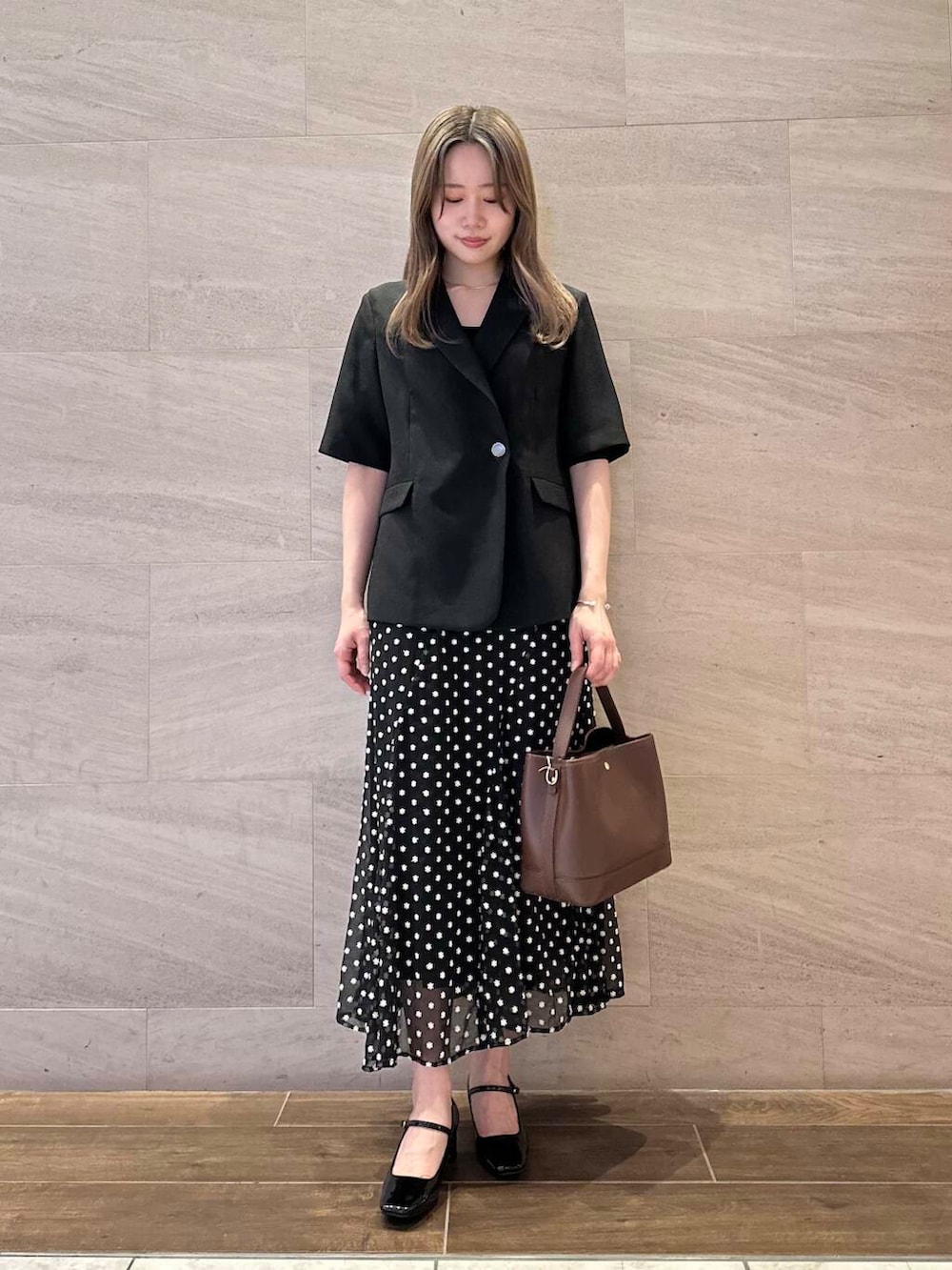 ブラック系のパンプス、ブラウン系のハンドバッグ、ブラック系のスカートを着用したレディースの春コーディネートの2枚目の写真
