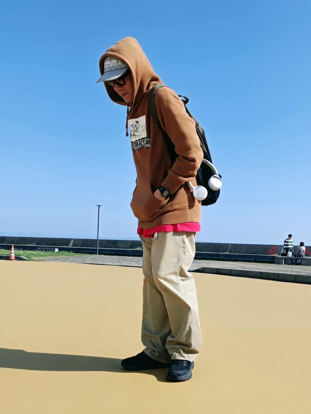 ブラウン系のパーカー、ベージュ系のチノパンツ、ブラック系のスニーカーを着用したメンズの春コーディネートの3枚目の写真