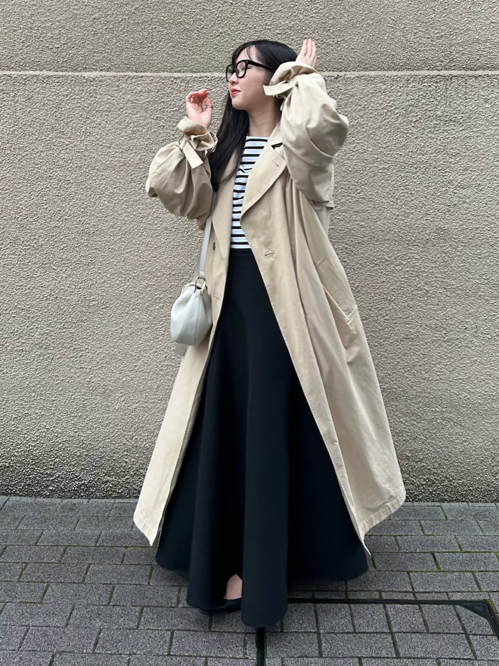 ホワイト系のショルダーバッグ、ブラック系のスカート、ベージュ系のトレンチコートを着用したレディースの春コーディネートの2枚目の写真