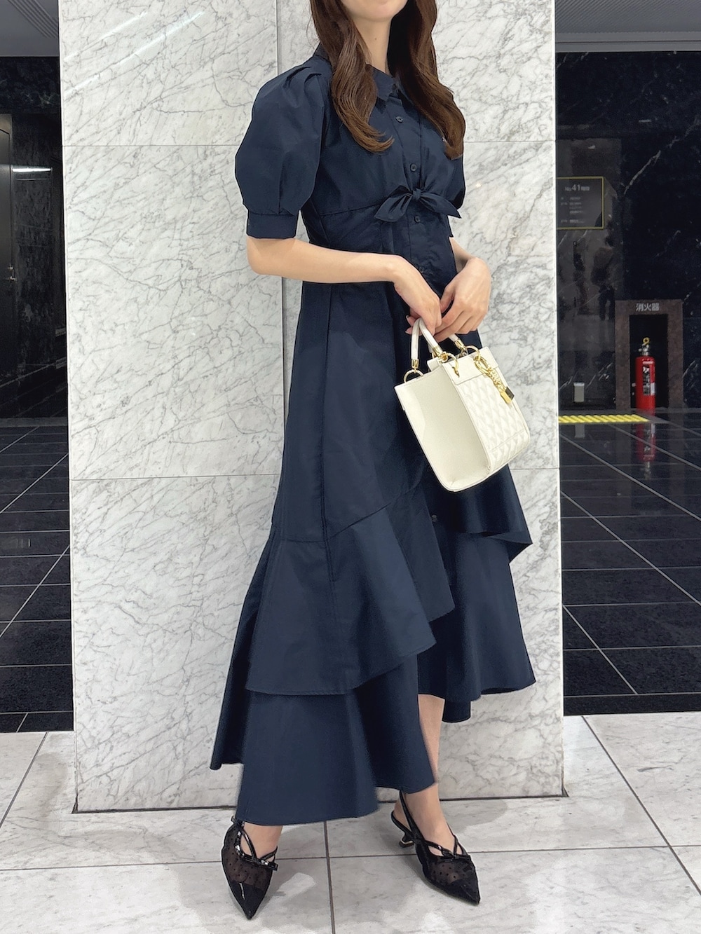 ブルー系のワンピース、ホワイト系のハンドバッグ、ブラック系のパンプスを着用したレディースの春コーディネートの2枚目の写真