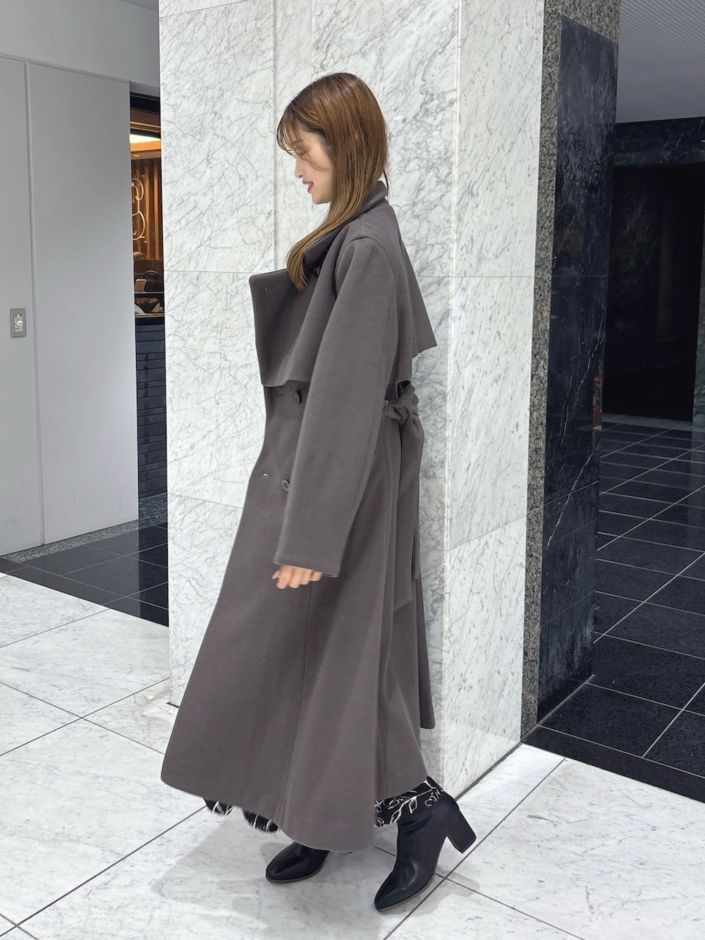 ブラック系のワンピース、ブラウン系のトレンチコート、ブラック系のブーツを着用したレディースの秋コーディネートの4枚目の写真