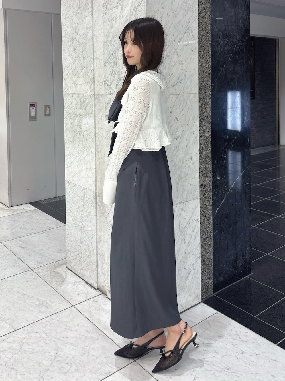 グレー系のワンピース、ホワイト系のカーディガン/ボレロ、ブラック系のパンプスを着用したレディースの春コーディネートの2枚目の写真