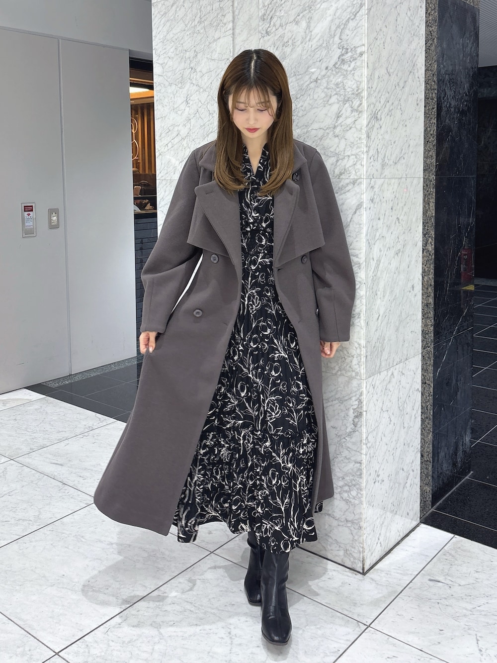 ブラック系のワンピース、ブラウン系のトレンチコート、ブラック系のブーツを着用したレディースの秋コーディネートの2枚目の写真