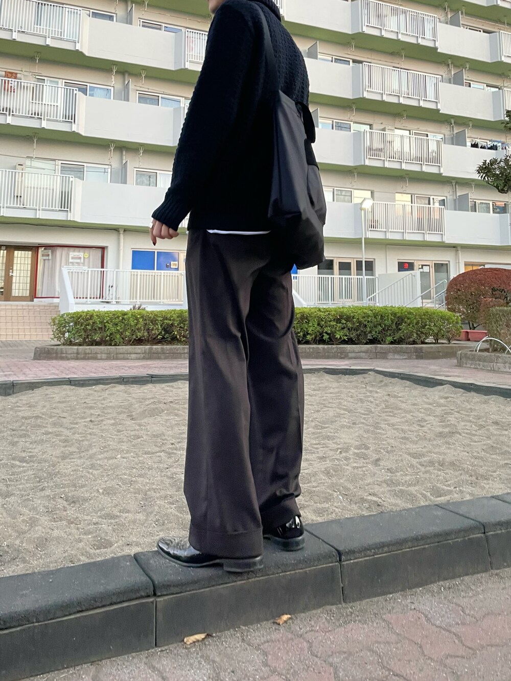 ブラック系のニット/セーター、ブラウン系のスラックスを着用したメンズの秋コーディネートの2枚目の写真