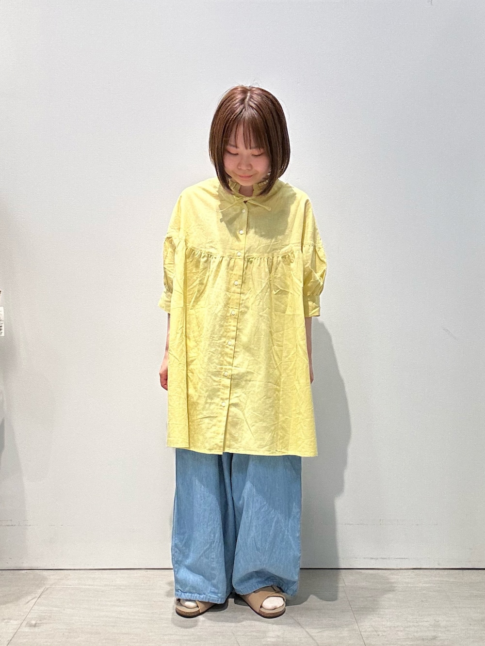 イエロー系のチュニック、ベージュ系のバッグ、ブルー系のデニムパンツを着用したレディースの夏コーディネートの2枚目の写真