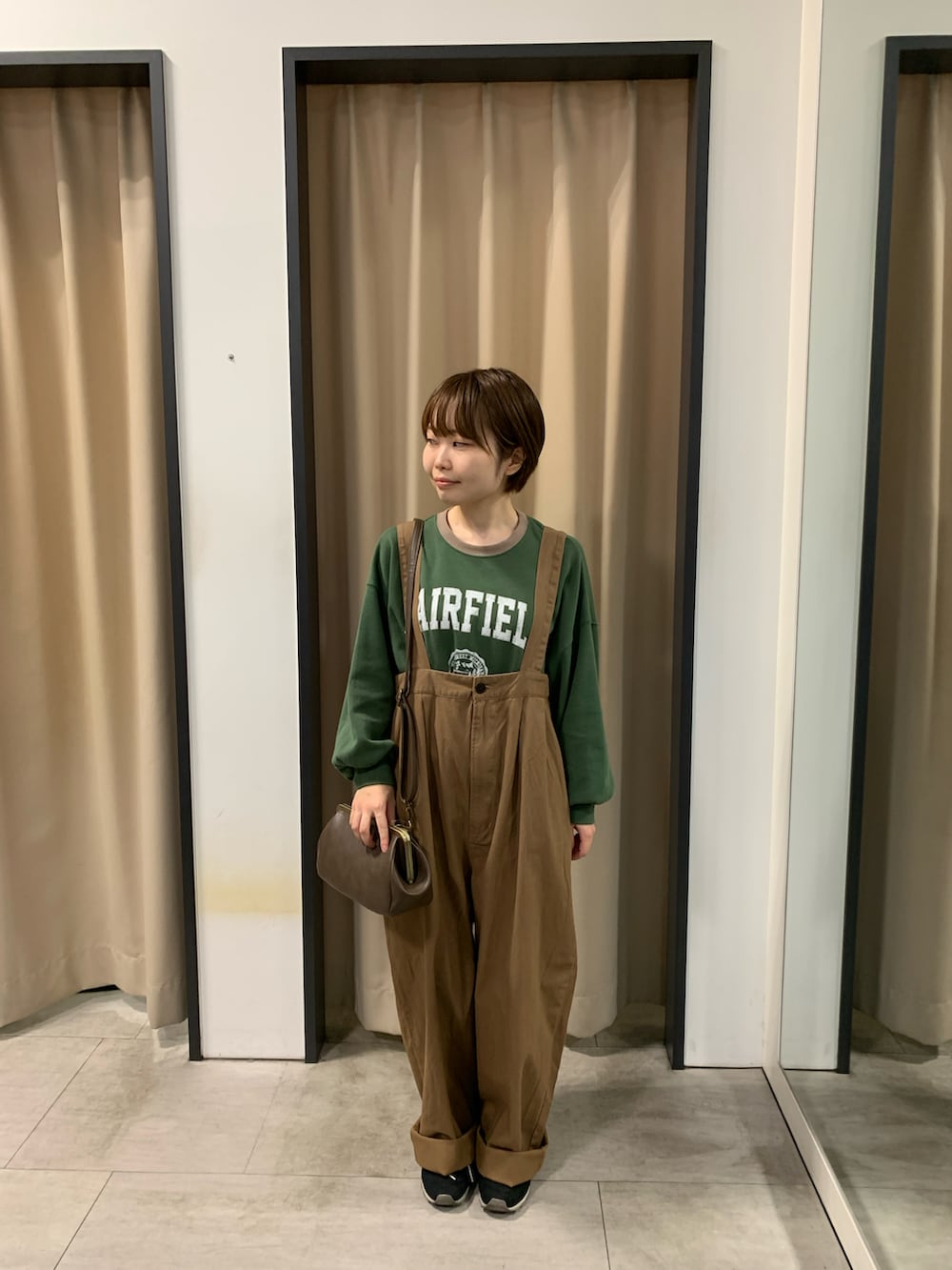 ブラウン系のサロペット/オーバーオール、グリーン系のTシャツ/カットソー、ブラウン系のハンドバッグを着用したレディースの秋コーディネートの2枚目の写真