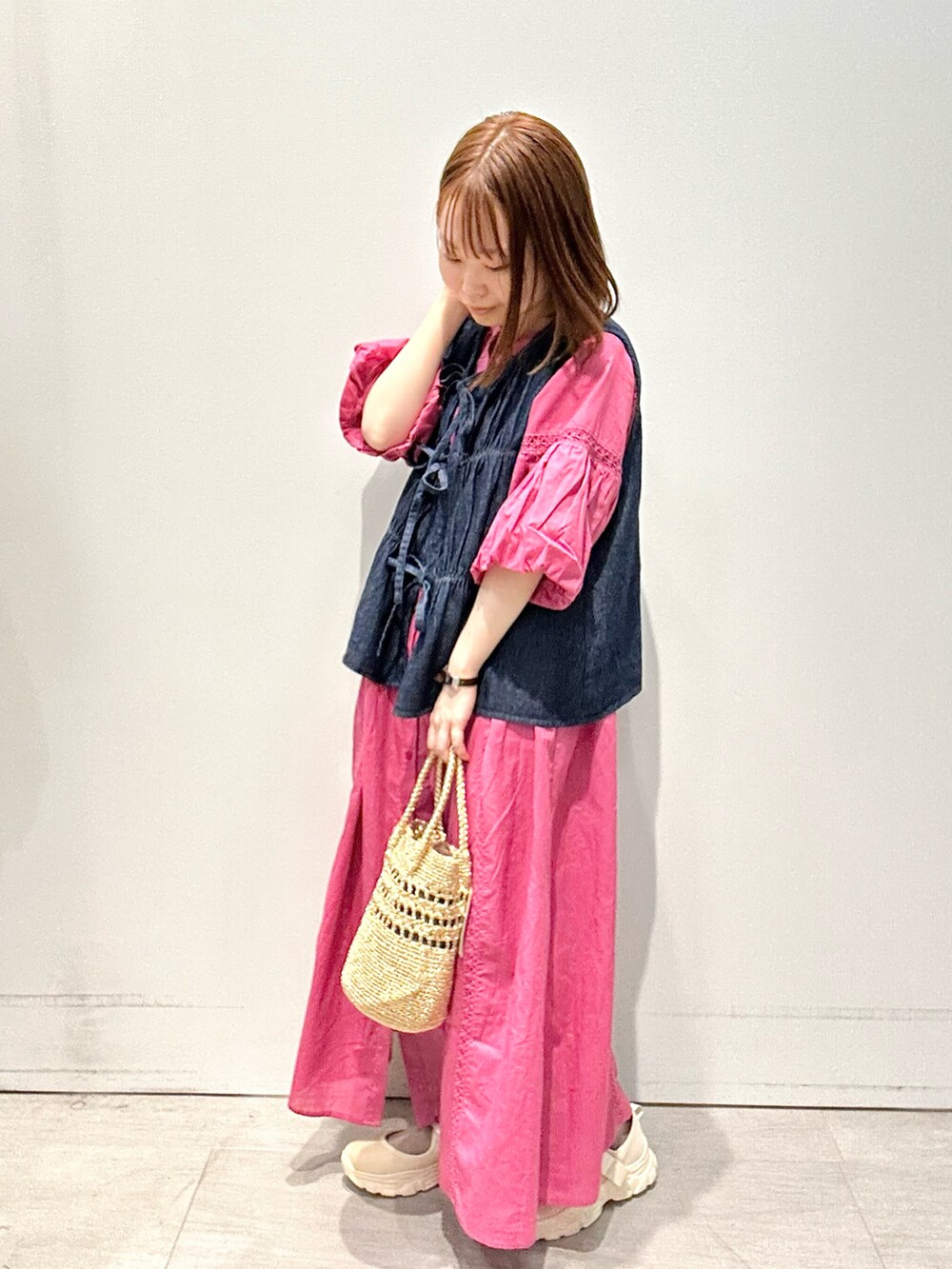 ブルー系のベスト、ピンク系のワンピース、ゴールド系のハンドバッグを着用したレディースの春コーディネートの2枚目の写真