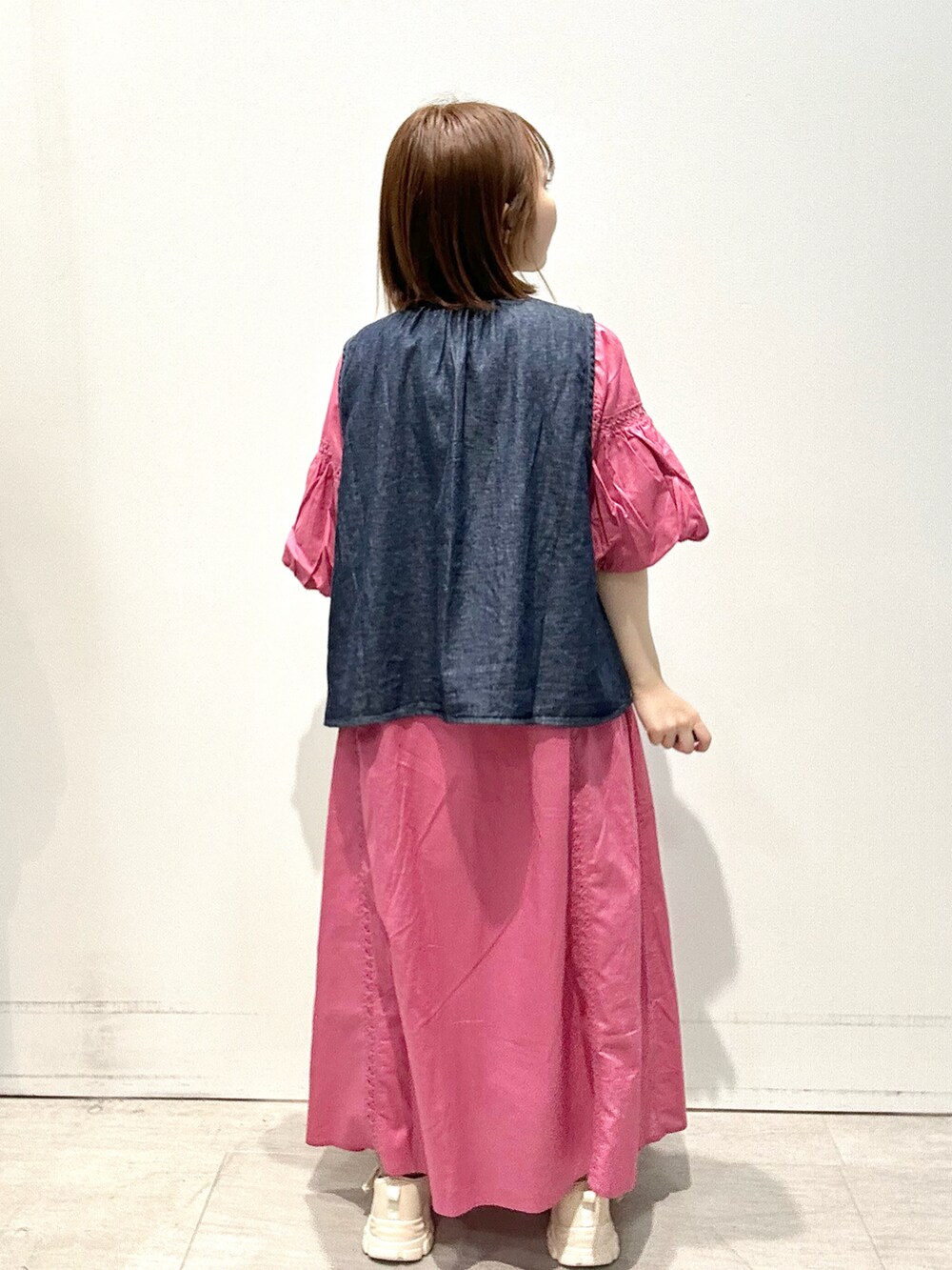 ブルー系のベスト、ピンク系のワンピース、ゴールド系のハンドバッグを着用したレディースの春コーディネートの3枚目の写真