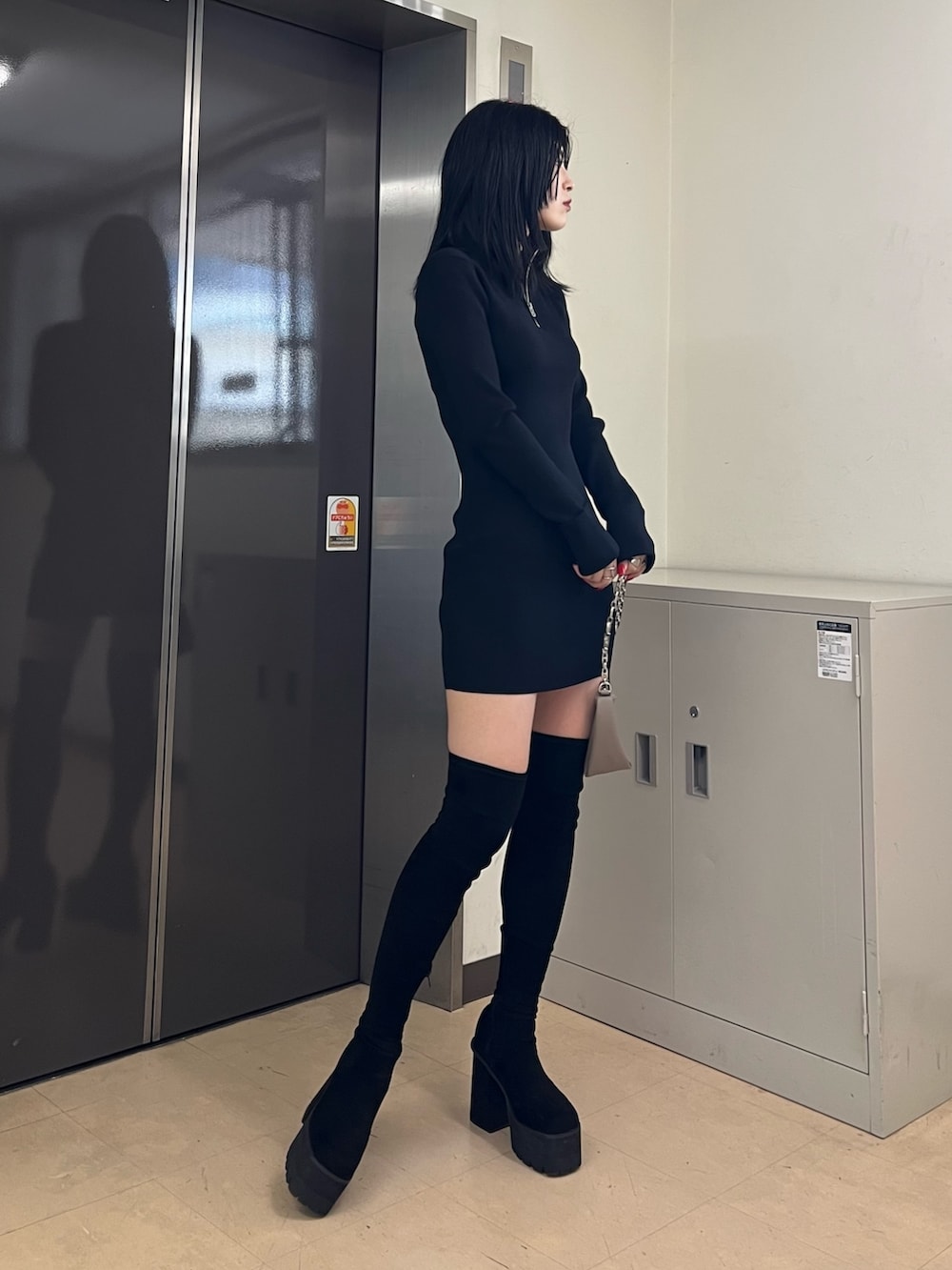 ブラック系のワンピース、ベージュ系のハンドバッグ、ブラック系のブーツを着用したレディースの秋コーディネートの2枚目の写真