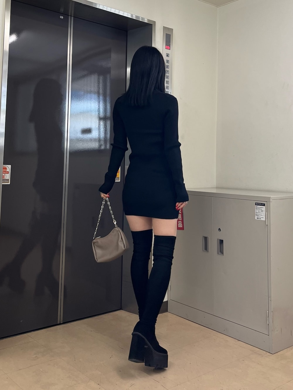 ブラック系のワンピース、ベージュ系のハンドバッグ、ブラック系のブーツを着用したレディースの秋コーディネートの3枚目の写真