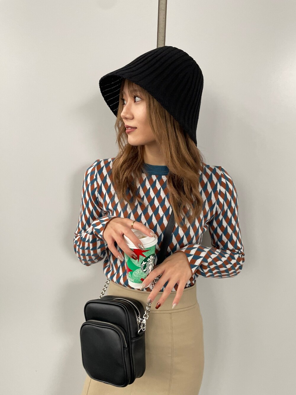 ブラック系のショルダーバッグ、オレンジ系のニット/セーター、ベージュ系のスカートを着用したレディースの秋コーディネートの5枚目の写真