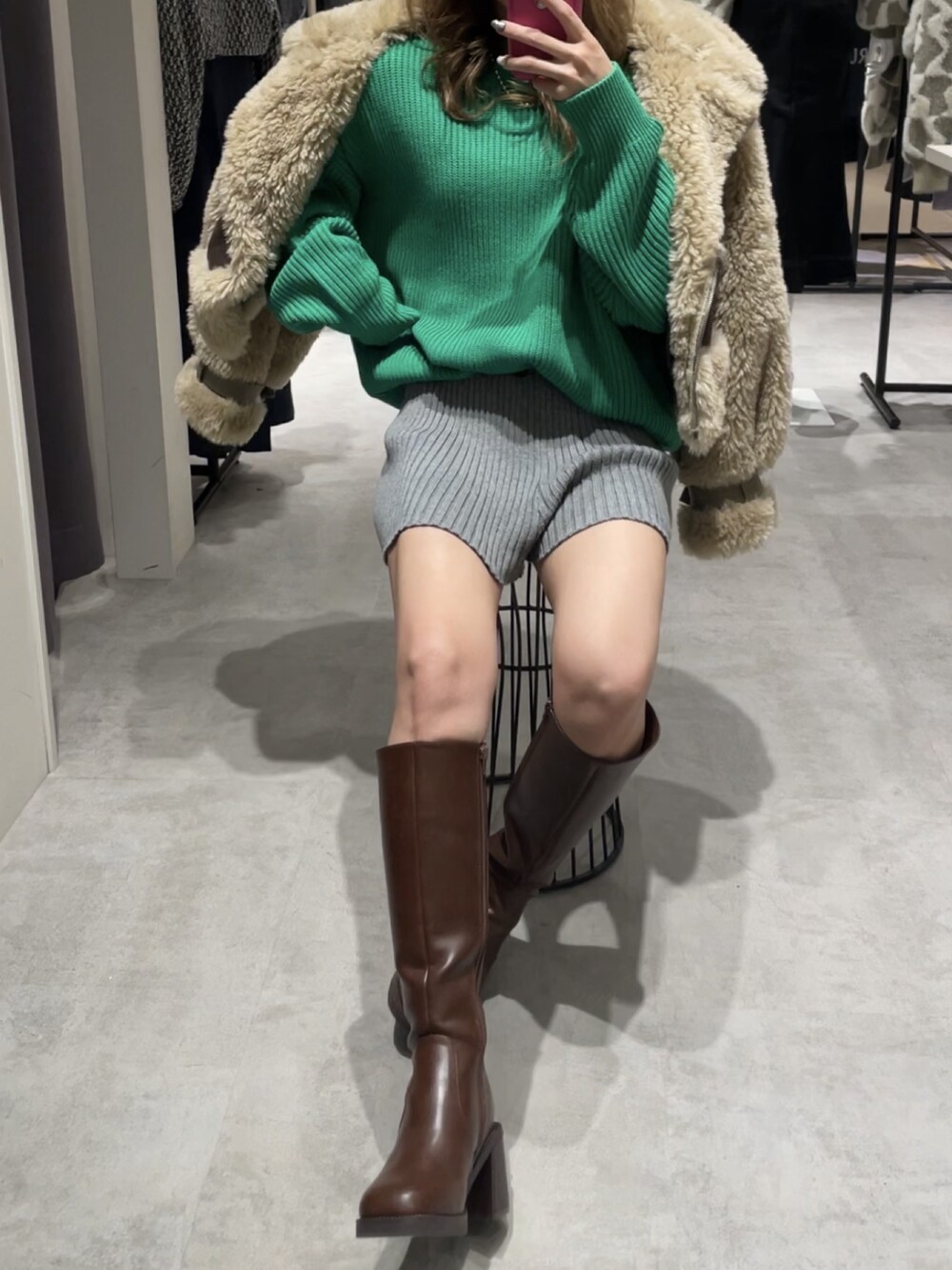 ブラウン系のムートンコート、グリーン系のニット/セーター、グレー系のスウェットパンツを着用したレディースの冬コーディネートの2枚目の写真