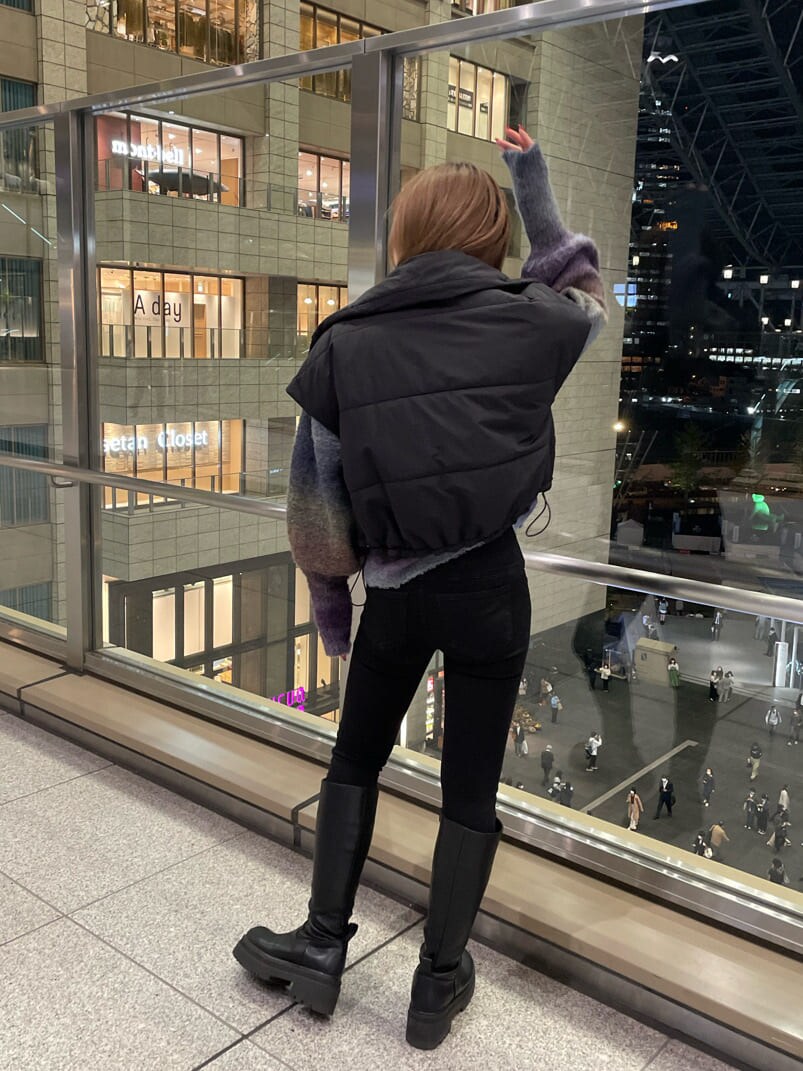 ブラック系のダウンベスト、ブラック系のブーツ、パープル系のニット/セーターを着用したレディースの秋コーディネートの2枚目の写真