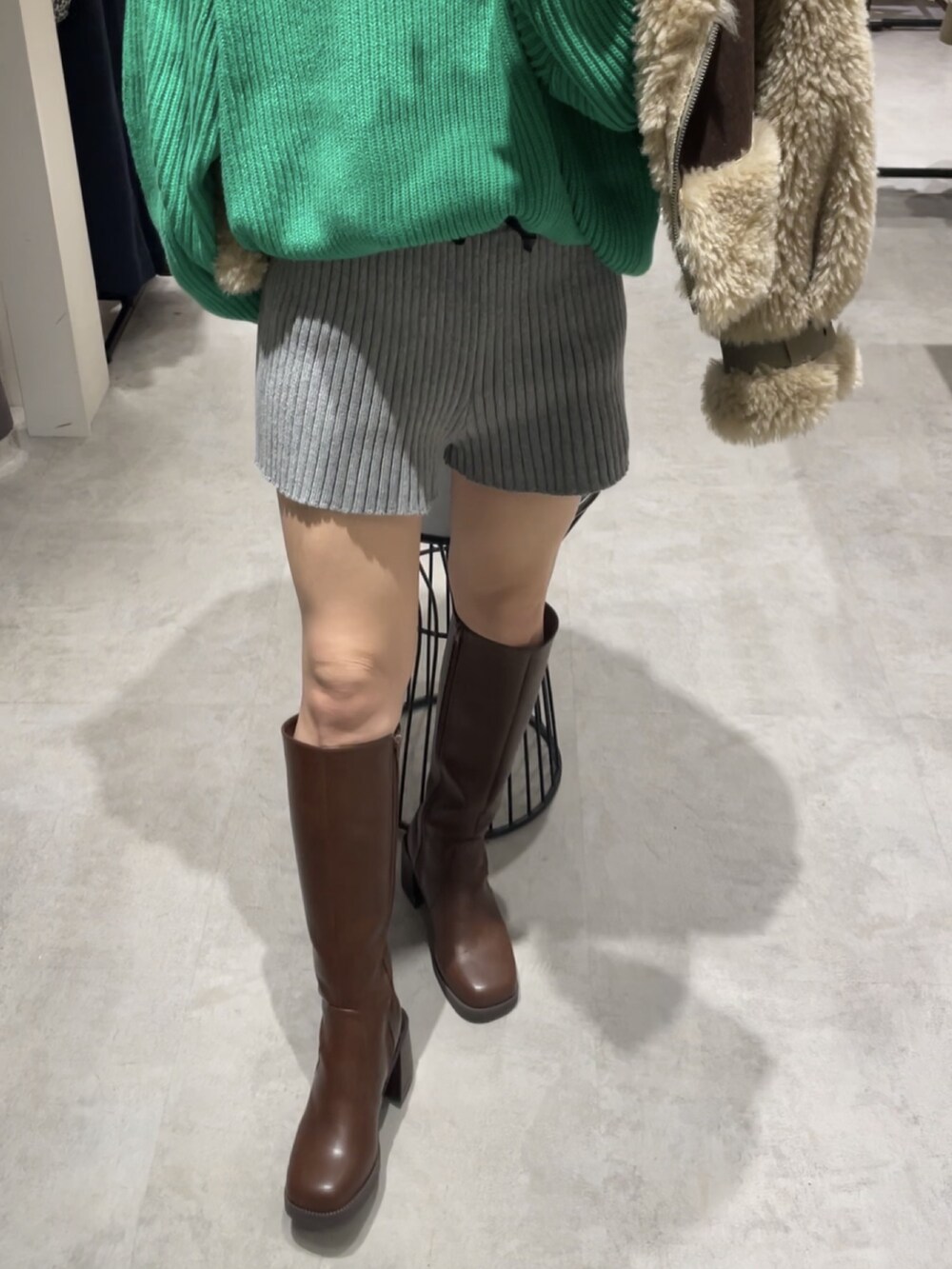 ブラウン系のムートンコート、グリーン系のニット/セーター、グレー系のスウェットパンツを着用したレディースの冬コーディネートの3枚目の写真