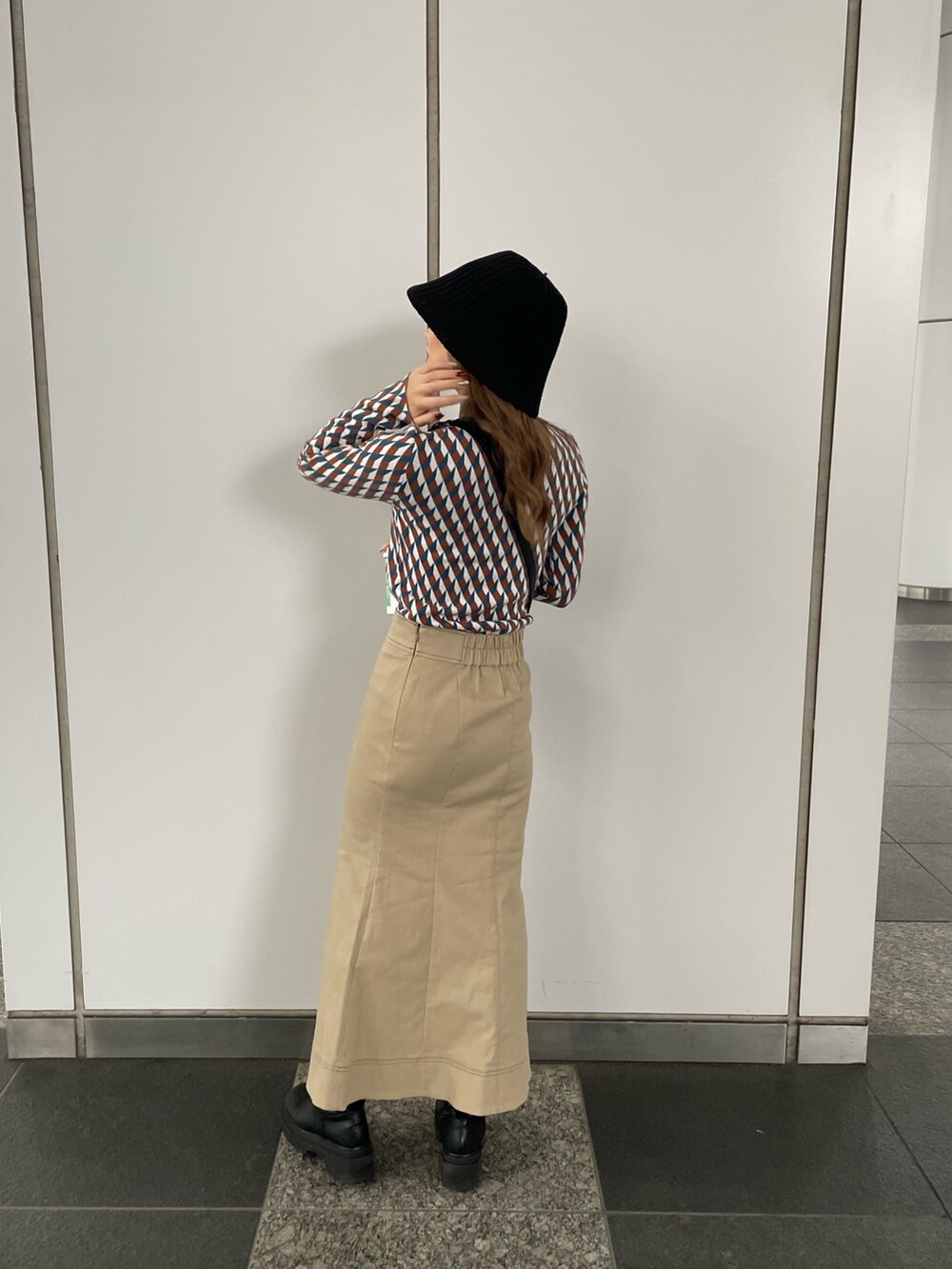 ブラック系のショルダーバッグ、オレンジ系のニット/セーター、ベージュ系のスカートを着用したレディースの秋コーディネートの3枚目の写真