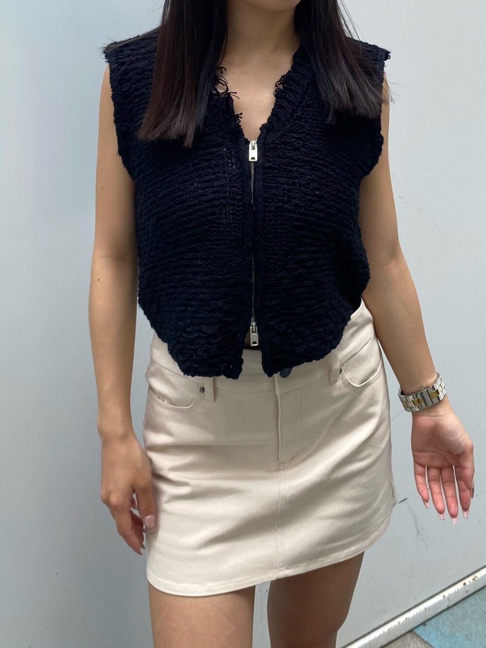 ホワイト系のベスト、ホワイト系のスカート、ブラック系のブーツを着用したレディースの夏コーディネートの2枚目の写真