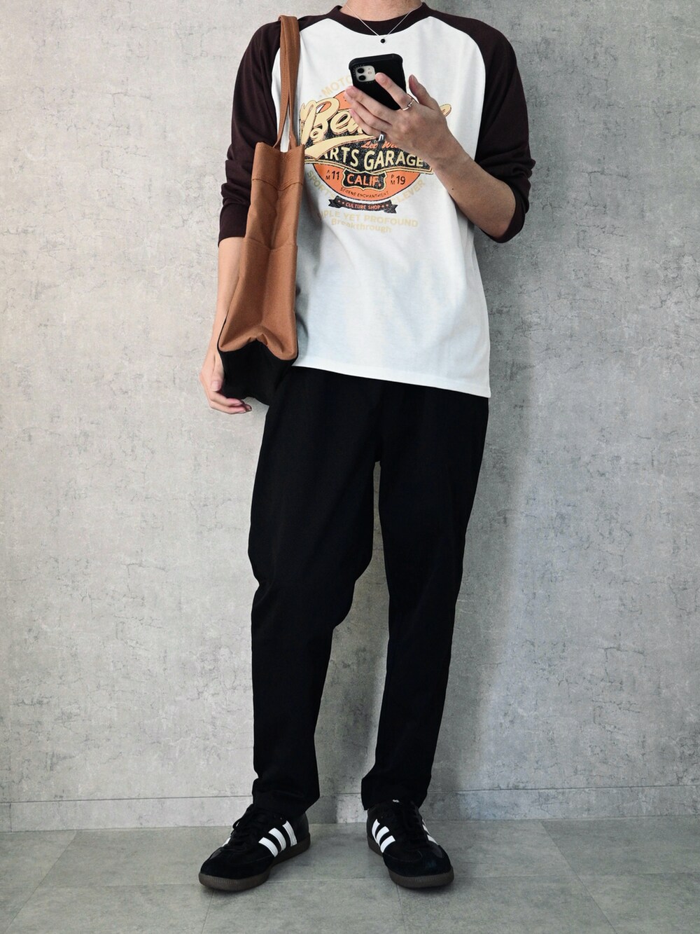 ブラック系のTシャツ/カットソー、ブラック系のチノパンツ、ブラウン系のトートバッグを着用したメンズの秋コーディネートの2枚目の写真