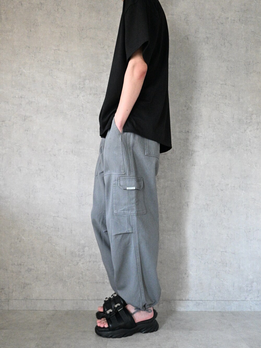 グレー系のカーゴパンツ、ブラック系のTシャツ/カットソー、ブラック系のサンダルを着用したメンズの夏コーディネートの2枚目の写真