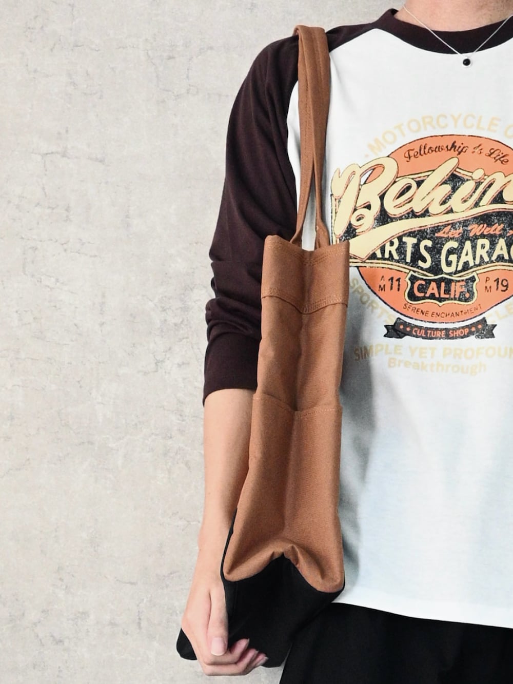 ブラック系のTシャツ/カットソー、ブラック系のチノパンツ、ブラウン系のトートバッグを着用したメンズの秋コーディネートの3枚目の写真