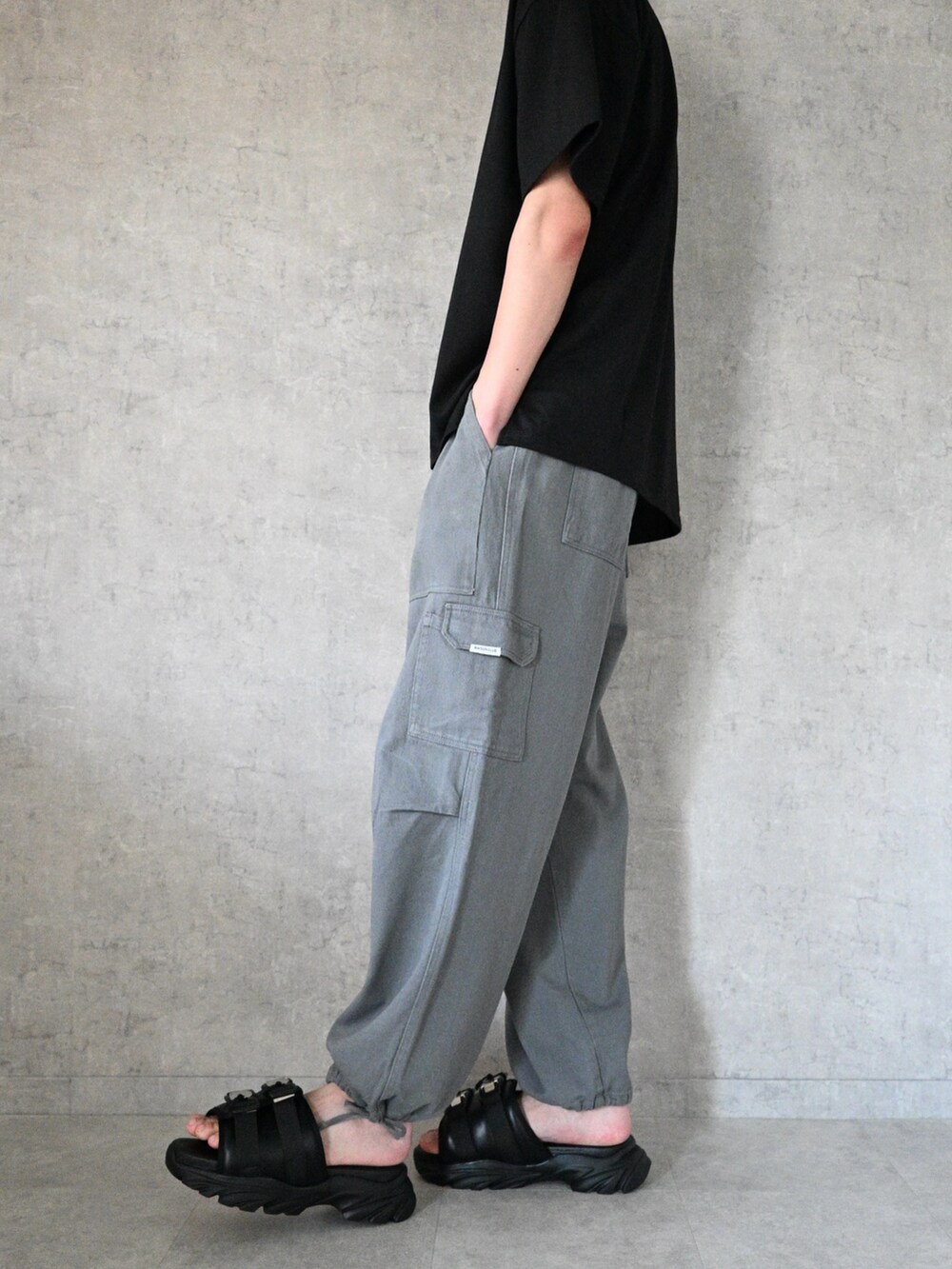 グレー系のカーゴパンツ、ブラック系のTシャツ/カットソー、ブラック系のサンダルを着用したメンズの夏コーディネートの3枚目の写真