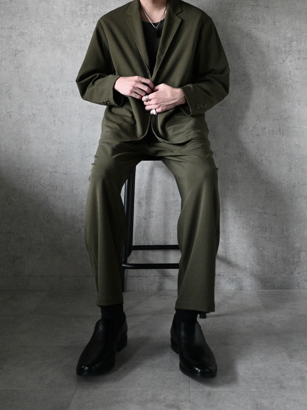 グリーン系のセットアップ、ブラック系のローファー、ブラック系のネックレスを着用したメンズの秋コーディネートの2枚目の写真