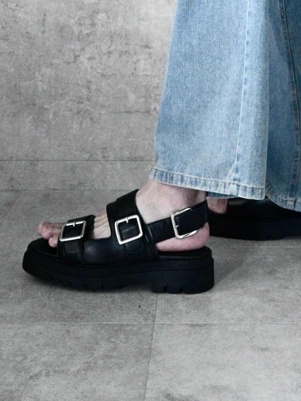 ブラック系のサンダル、ブラック系のTシャツ/カットソー、ブルー系のデニムパンツを着用したメンズの夏コーディネートの2枚目の写真