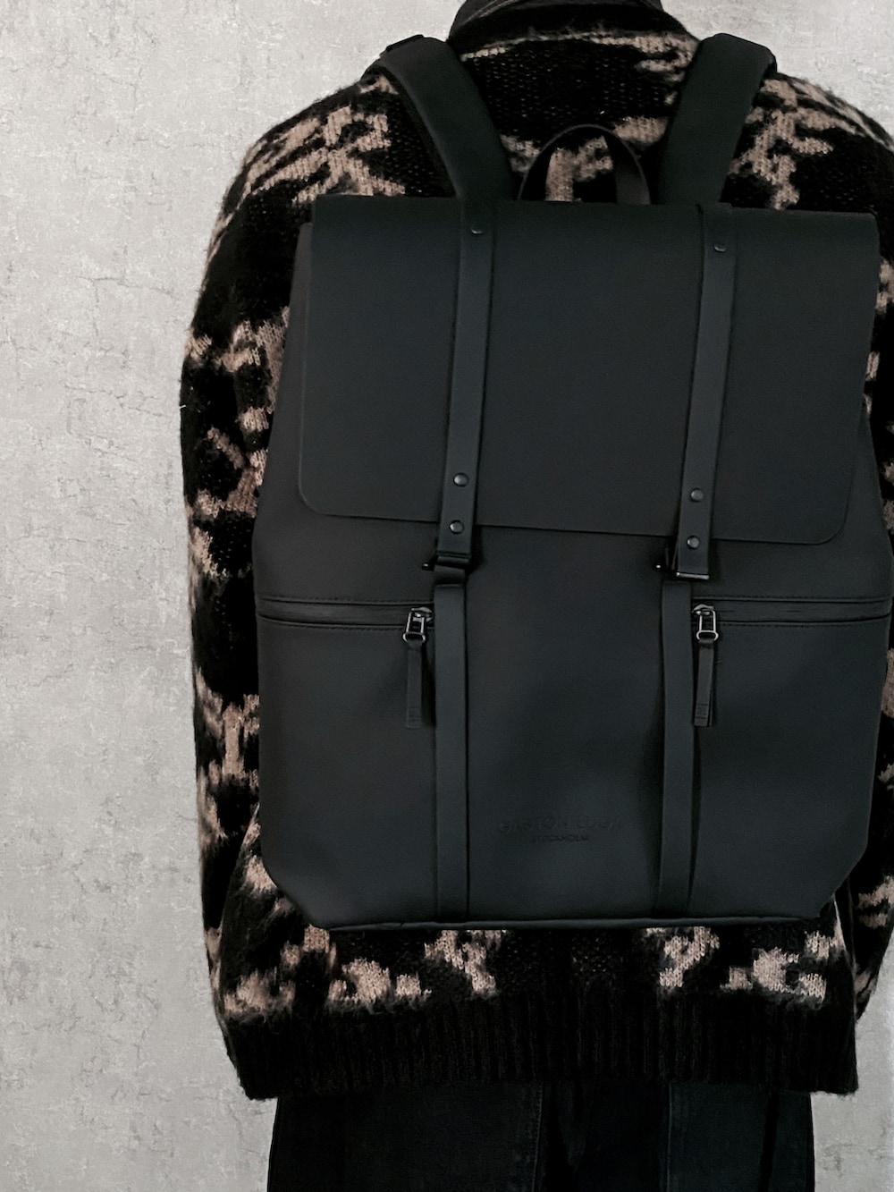 ブラック系のバックパック/リュック、ブラック系のカーディガン/ボレロ、ブラック系のデニムパンツを着用したメンズの秋コーディネートの2枚目の写真