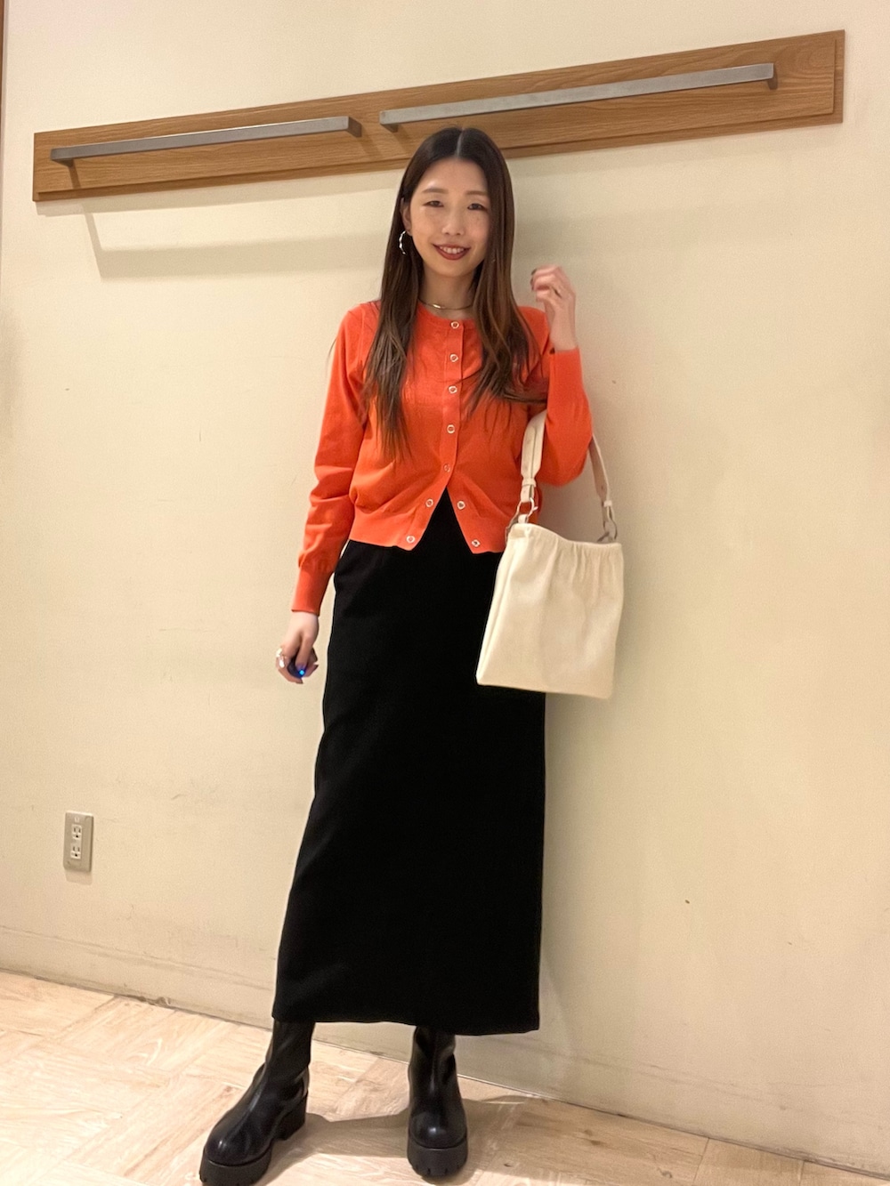 オレンジ系のカーディガン/ボレロ、ブラック系のスカートを着用したレディースの春コーディネートの2枚目の写真