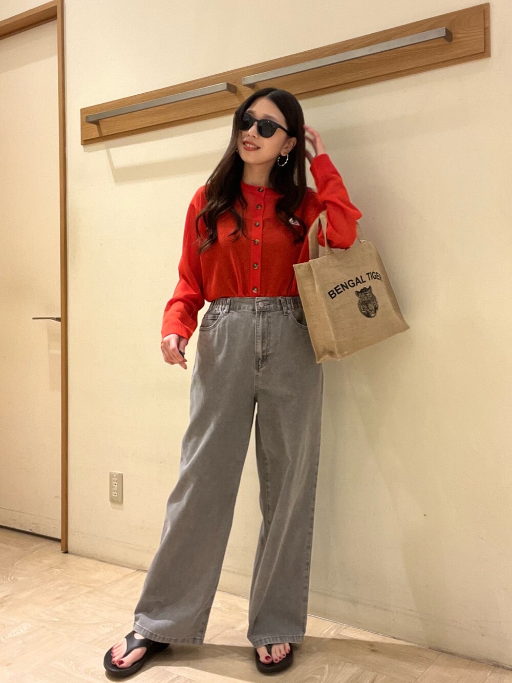 グレー系のデニムパンツ、レッド系のカーディガン/ボレロ、ベージュ系のトートバッグを着用したレディースの春コーディネートの3枚目の写真
