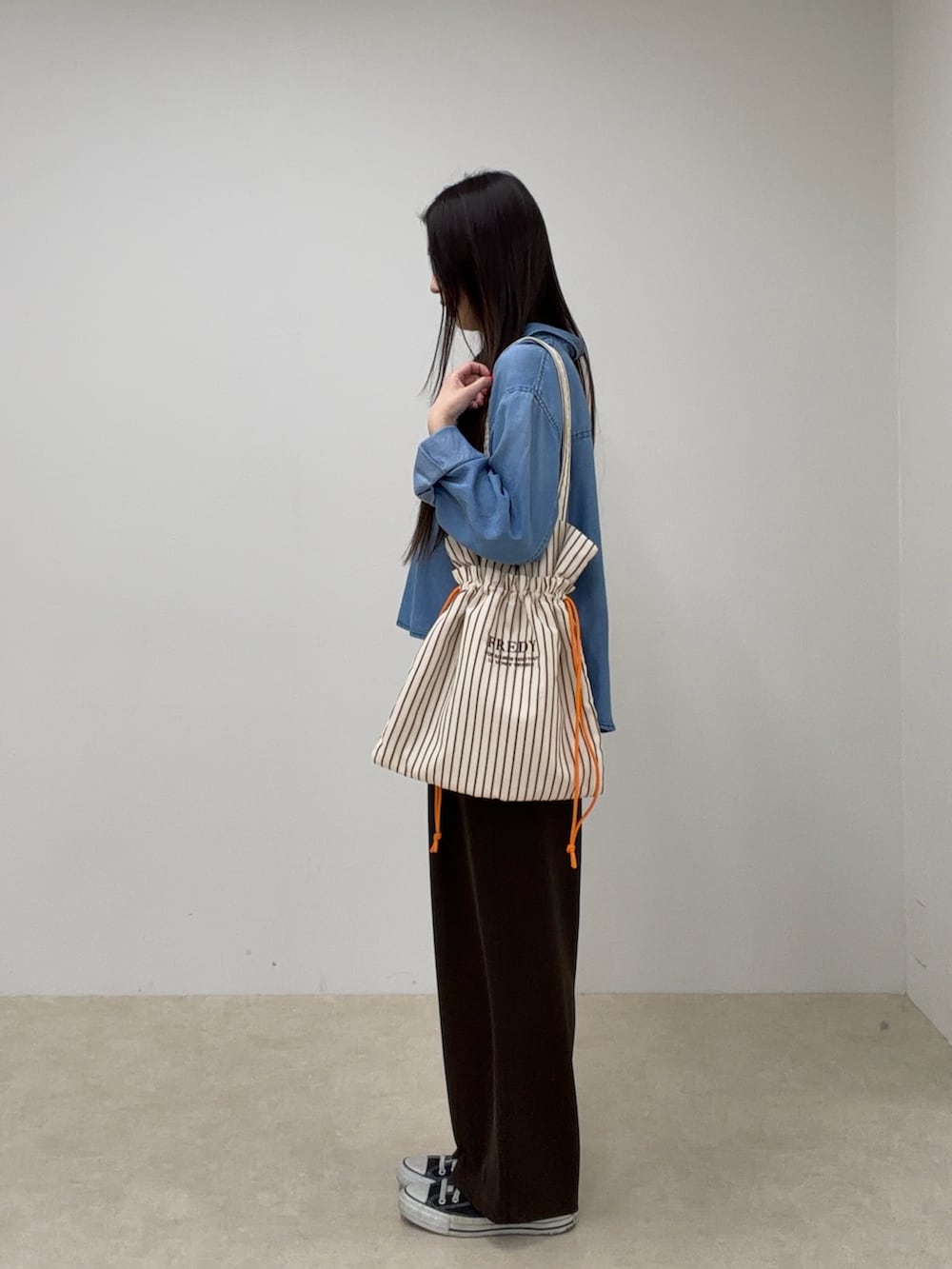 ブルー系のシャツ/ブラウス、ブラウン系のスラックス、レッド系のトートバッグを着用したレディースの春コーディネートの2枚目の写真