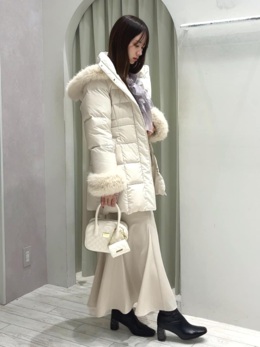 ホワイト系のハンドバッグ、ブラック系のブーツ、ホワイト系のダウンジャケット/コートを着用したレディースの秋コーディネートの3枚目の写真