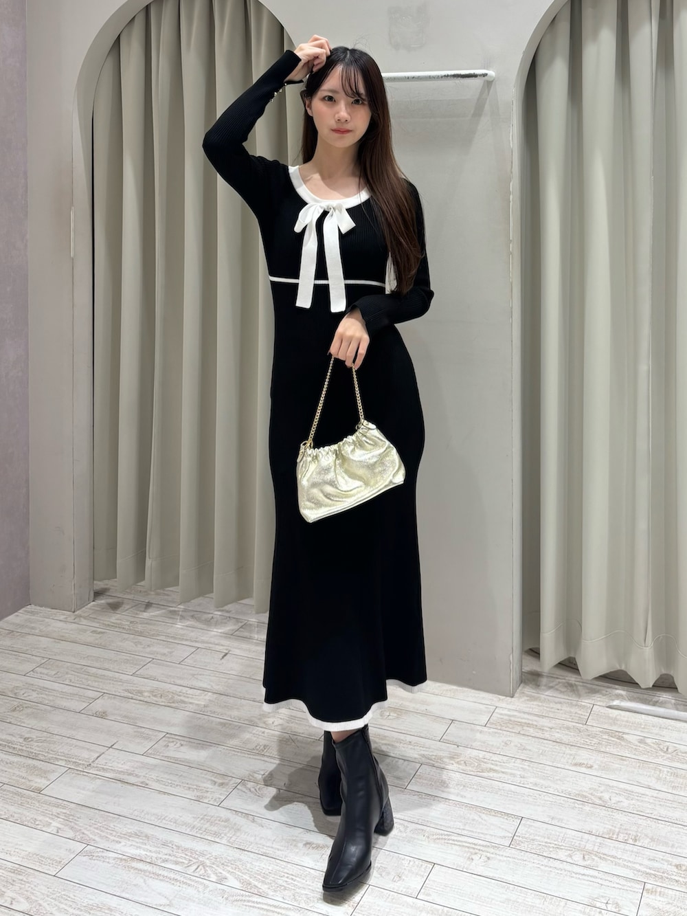 ブラック系のワンピース、ゴールド系のショルダーバッグ、ブラック系のブーツを着用したレディースの冬コーディネートの2枚目の写真