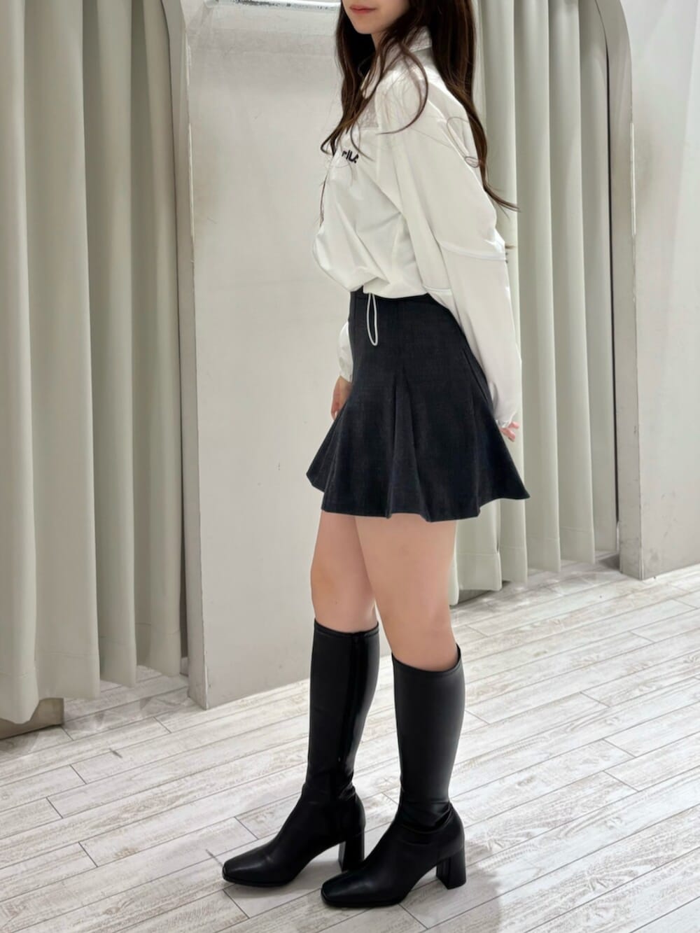 ブラック系のブーツ、ホワイト系のナイロンジャケット、グレー系のスカートを着用したレディースの冬コーディネートの3枚目の写真