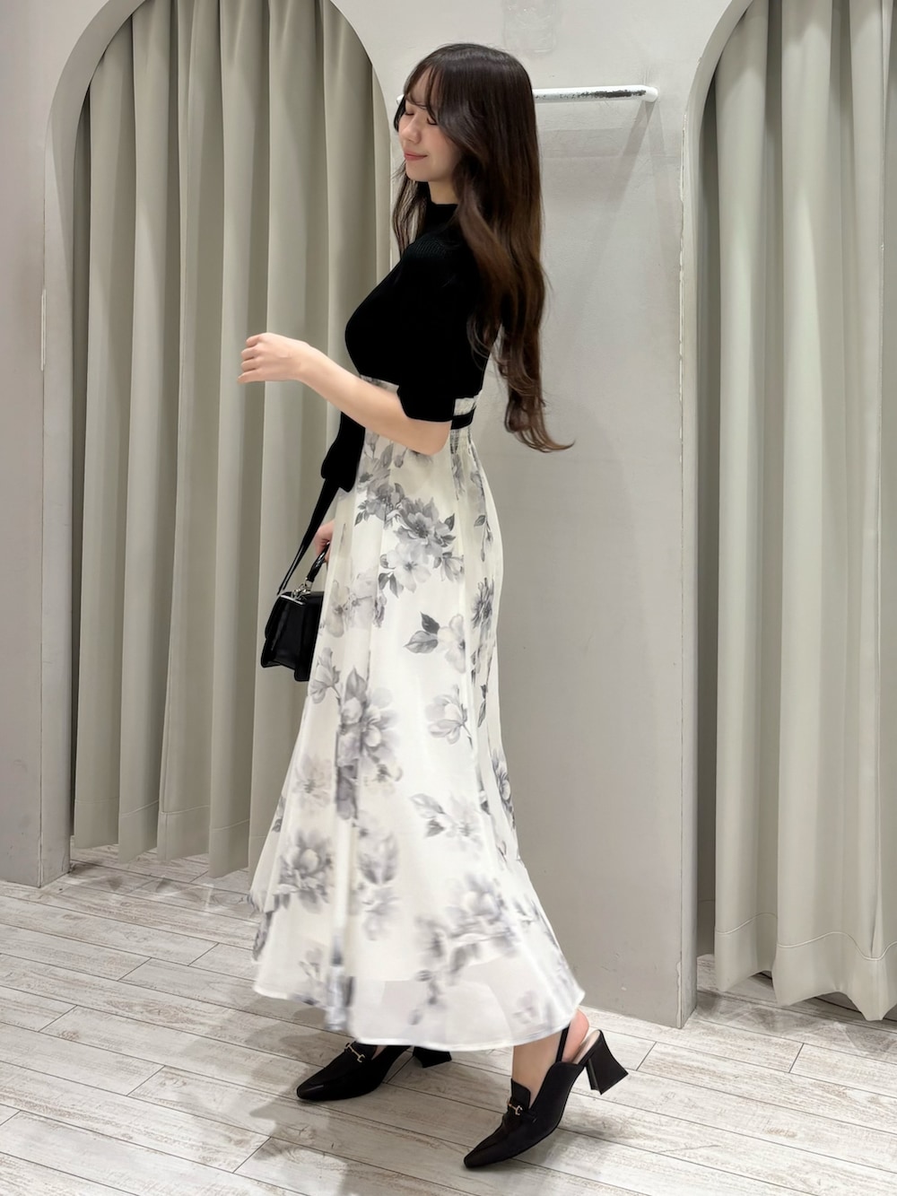 ブラック系のワンピース、ブラウン系のパンプス、ブラック系のハンドバッグを着用したレディースの春コーディネートの2枚目の写真