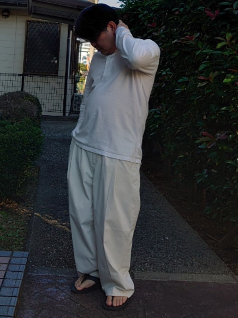 ホワイト系のTシャツ/カットソー、ホワイト系のスラックス、ブラック系のサンダルを着用したメンズの秋コーディネートの2枚目の写真