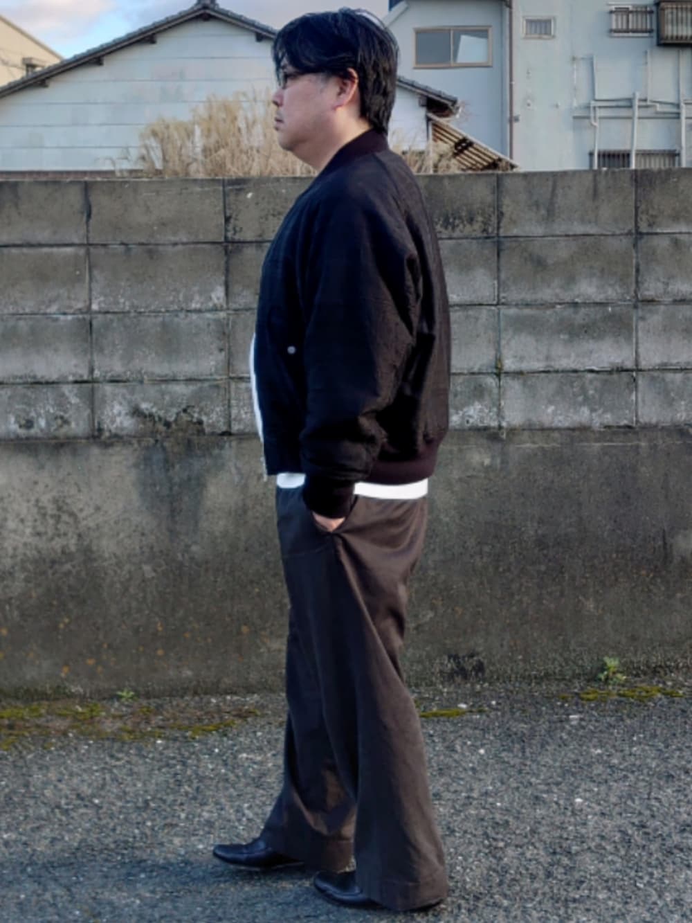 ブラック系のブルゾン、ホワイト系のニット/セーター、ブラック系のスラックスを着用したメンズの春コーディネートの2枚目の写真