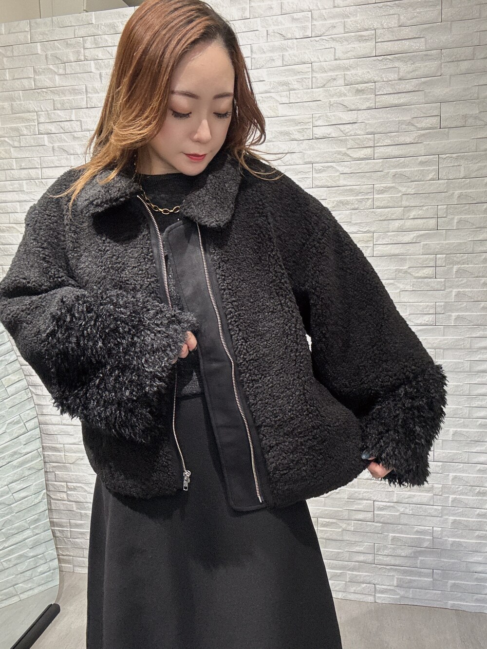 ブラック系のムートンコート、グレー系のニット/セーター、ブラック系のスカートを着用したレディースの冬コーディネートの3枚目の写真
